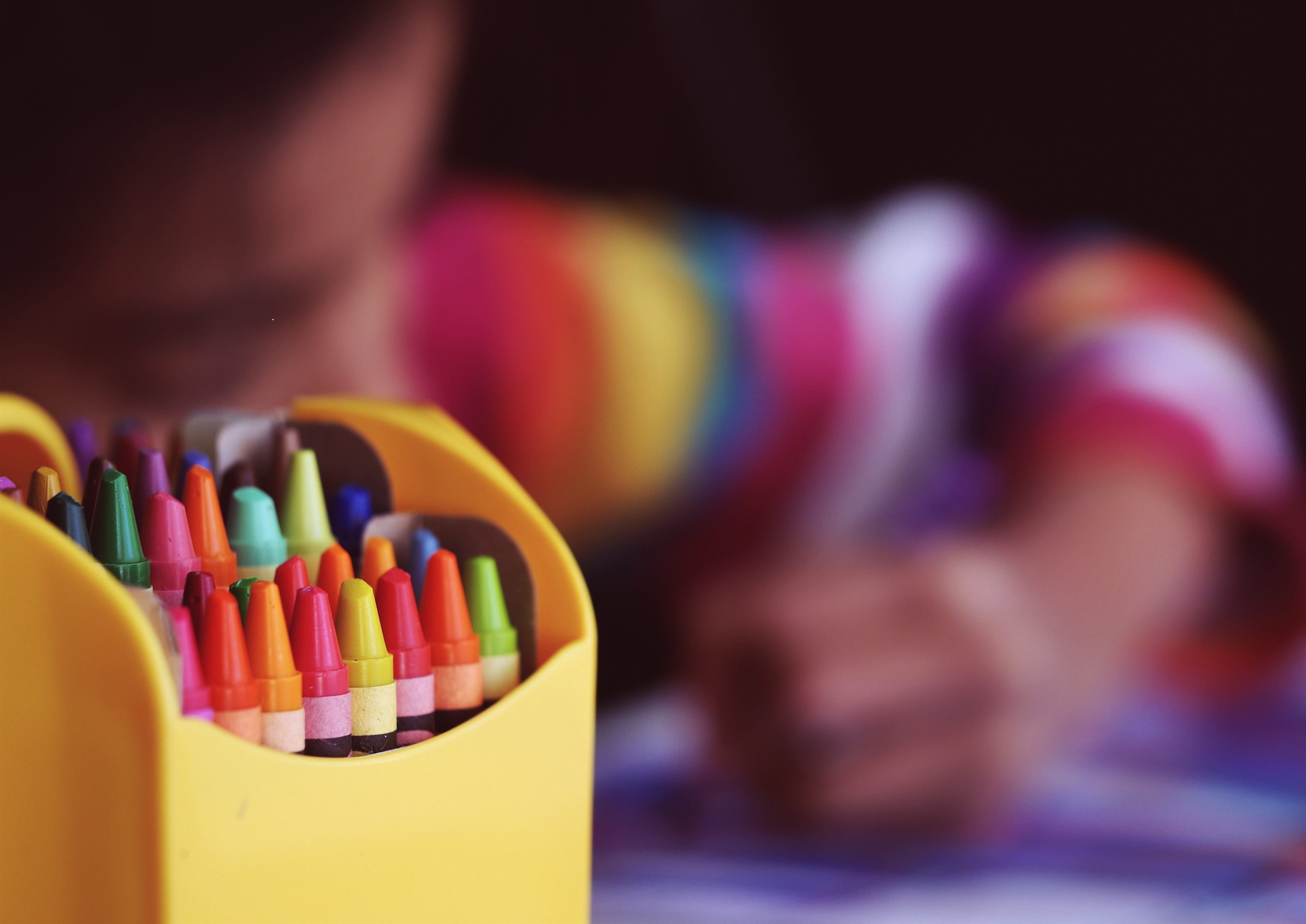 a child colouring in the background, with a pack of crayons in the forefront