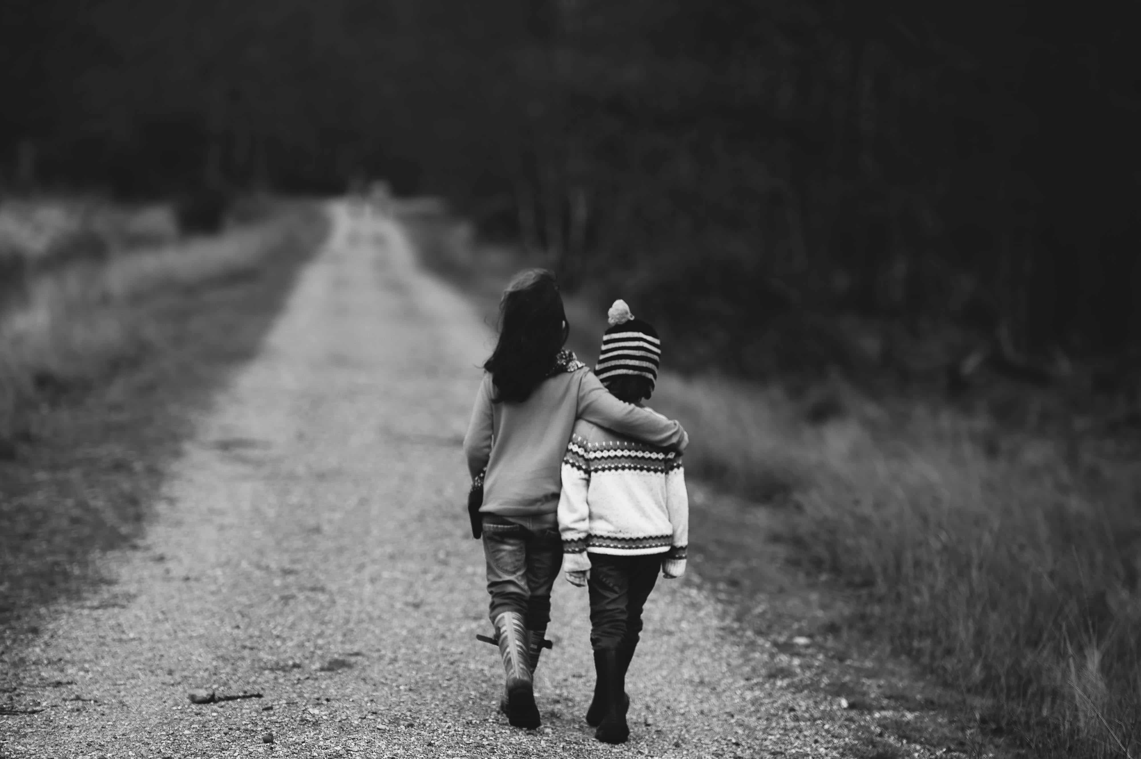 Two children walking down a road with an arm around each other