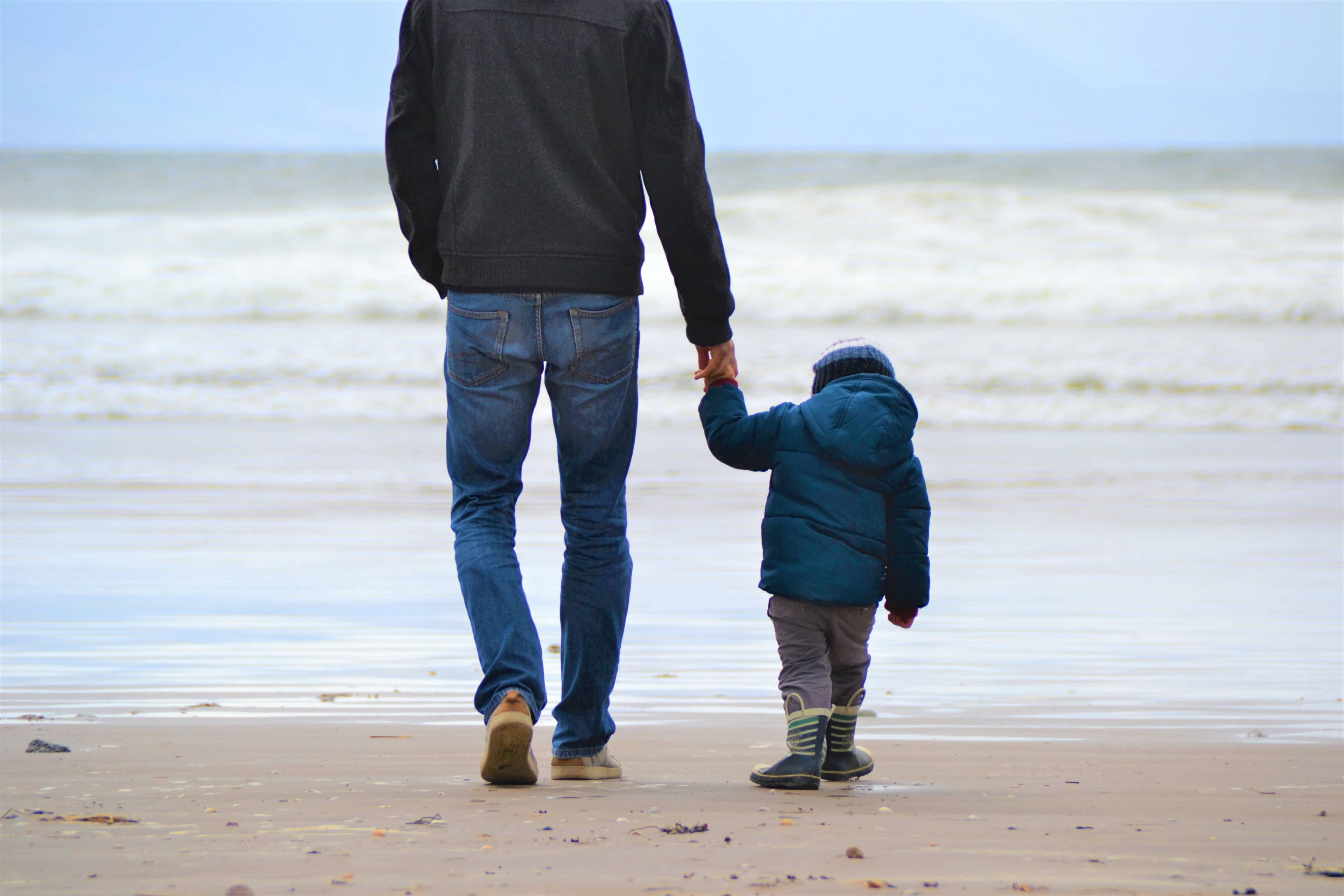 a man hand in hand with a young child on a beach representing a father's access to his son