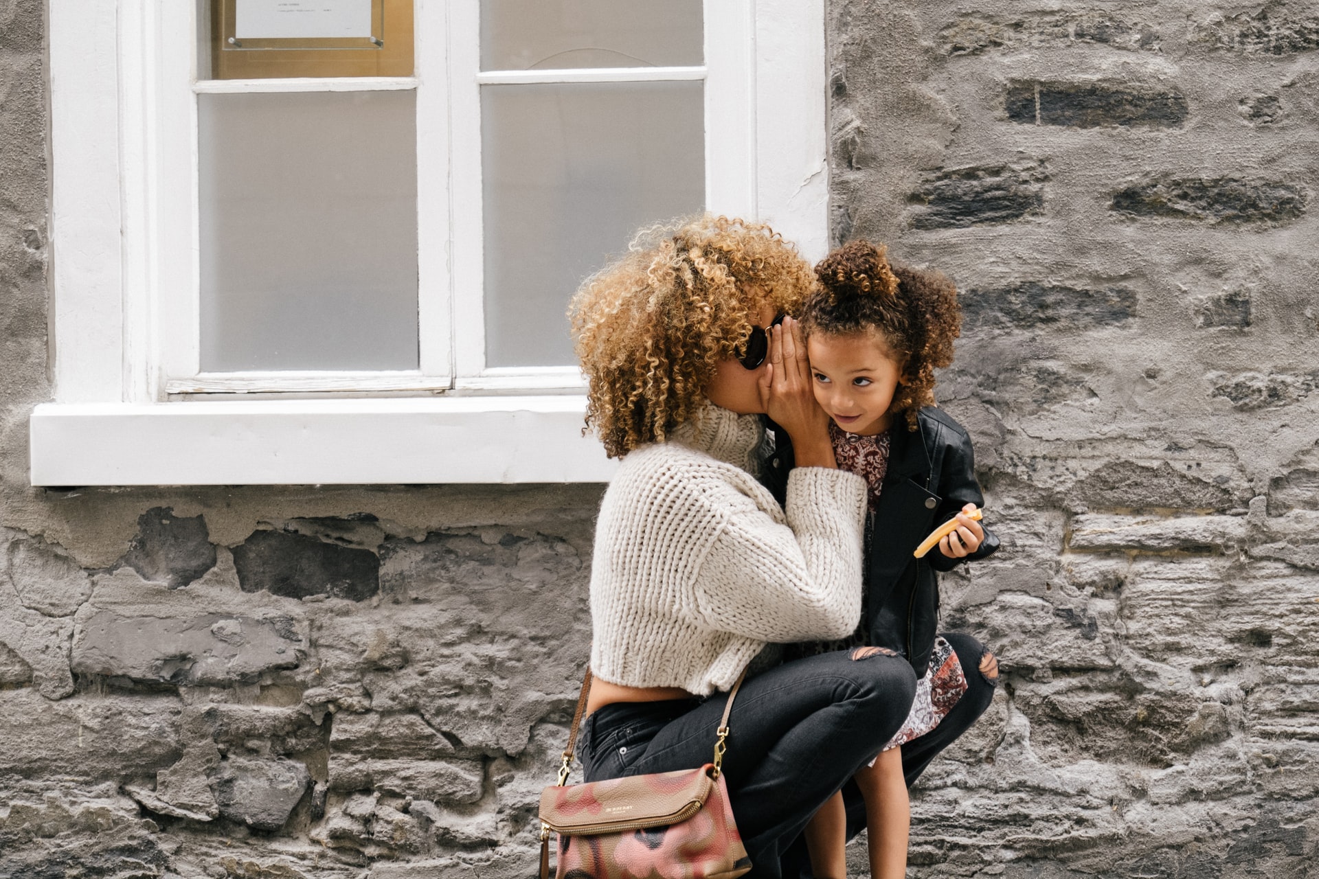 A mother whispering in her daughter's ear representing a parent trying to alienate their child from the other parent