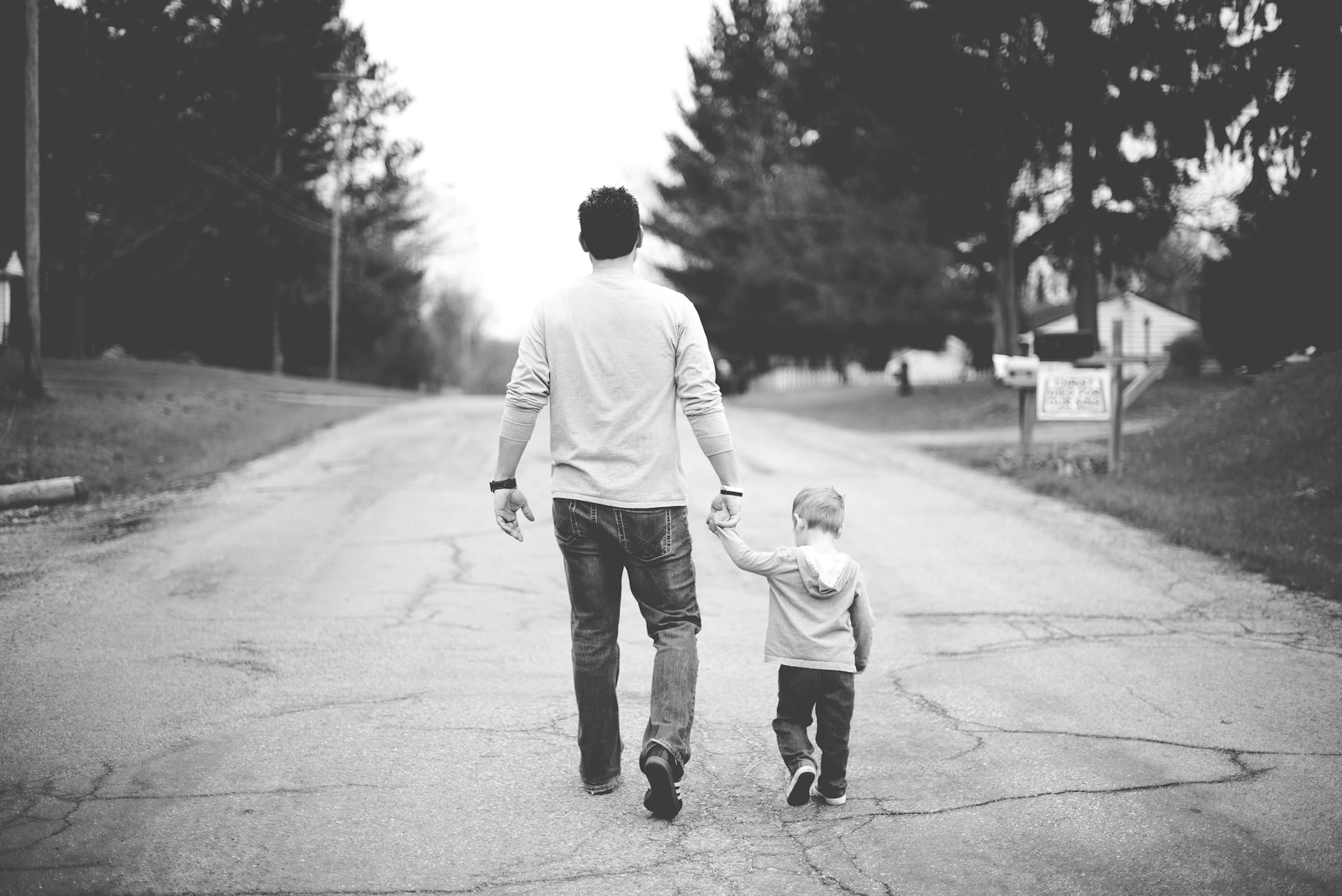 man holding childs hand walking down road