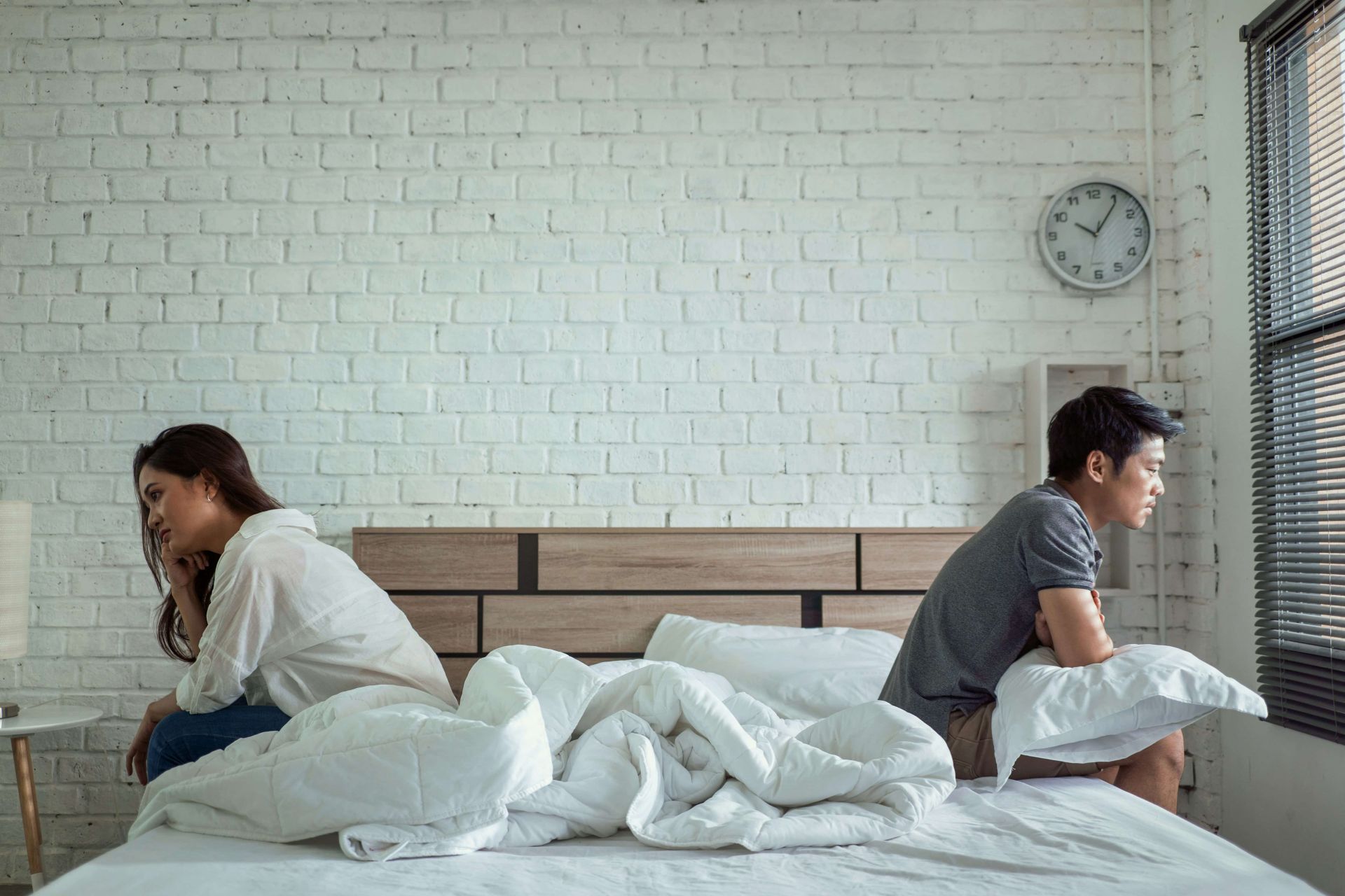 A man and woman facing away from each other, sitting on opposite sides of a bed, representing separation and the divorce process in Alberta