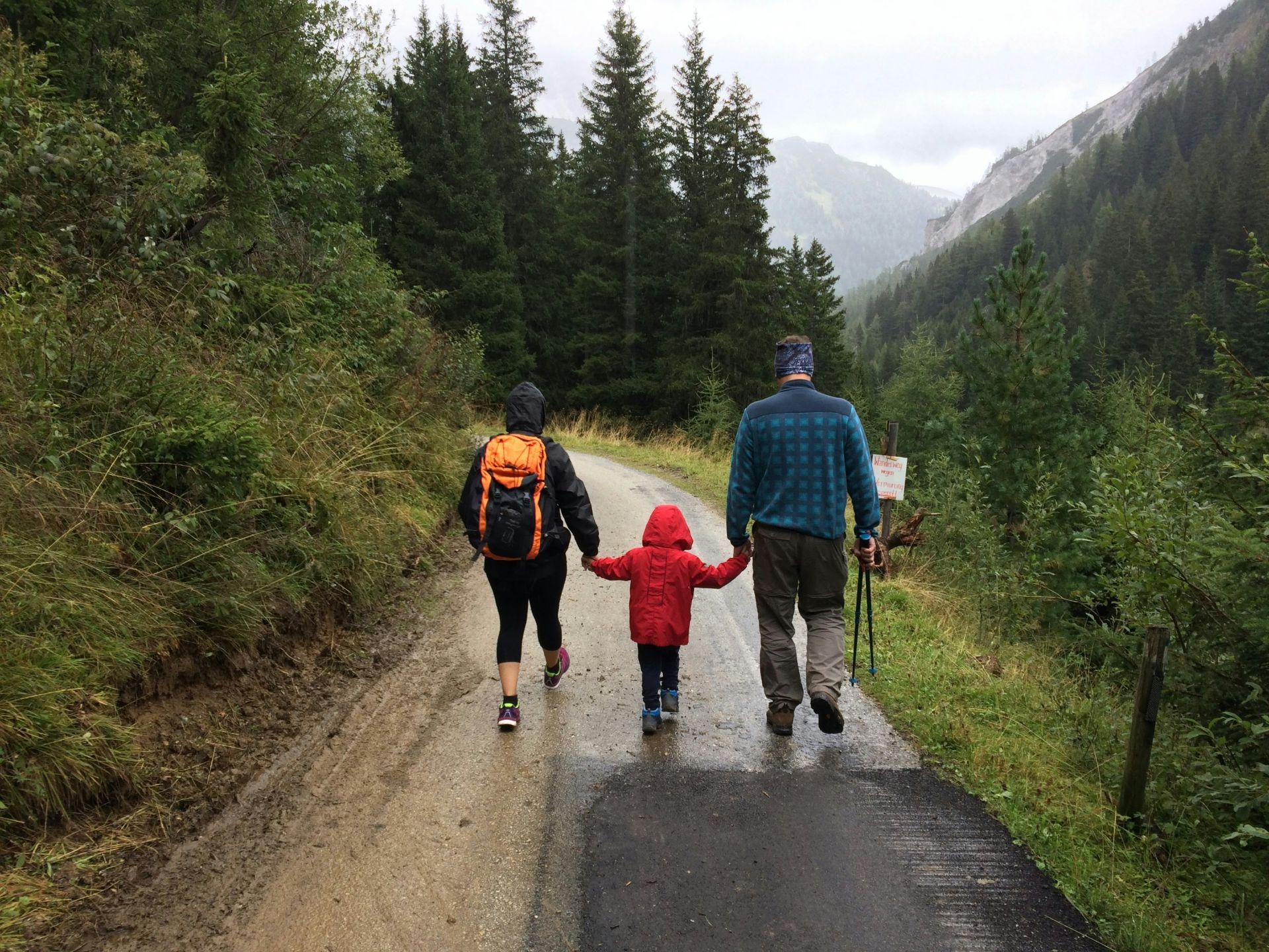 A man and woman holding hands with their child in between them while hiking a mountain path in the rain, representing shared parenting arrangements in Alberta
