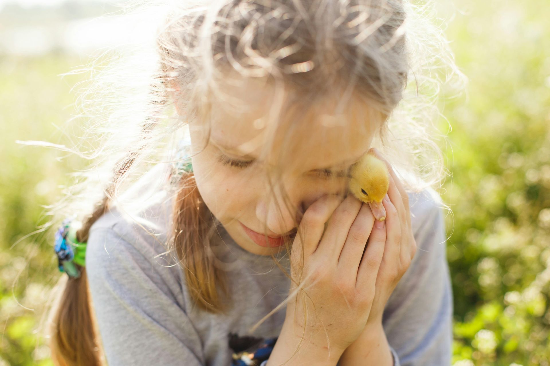 A child in need of protection, huddled happily in a green field with a baby chick in her hands.